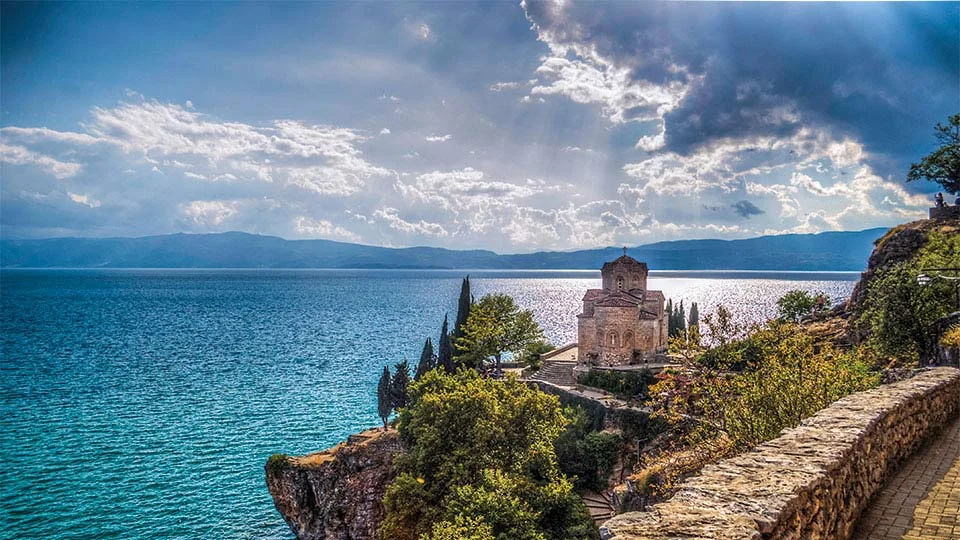 The church of St. John at Kaneo on a cliff above Lake Ohrid, with sunlight breaking through the clouds over the water